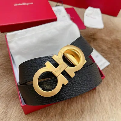 A black grained-leather belt coiled inside an open red presentation box, fastened with a large polished gold interlocking buckle
