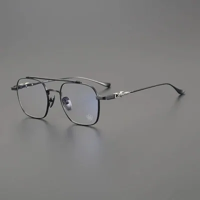 A pair of thin gunmetal metal-framed glasses with clear lenses and a double brow bar, photographed open against a plain grey background