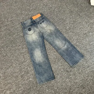One pair of wide-leg jeans laid on grey carpet, heavily faded pale blue denim with a small dark patch at the hip and an orange tag at the waistband