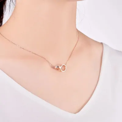 A fine rose-gold chain necklace worn on a model, with a small circular pendant resting just below the collarbone