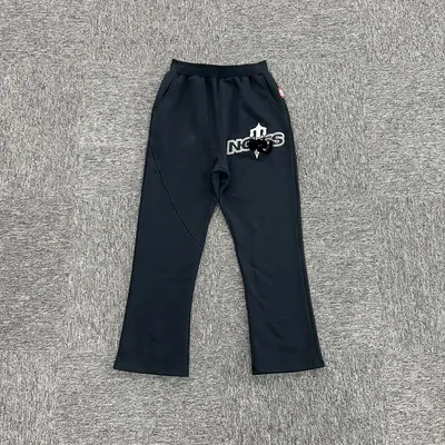 A pair of dark navy sweatpants laid flat on a grey background, slight flare at the ankle and a small light-coloured print high on the left leg