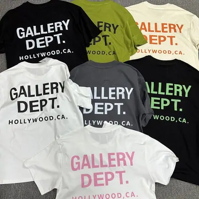 Seven short-sleeve t-shirts laid out and overlapping, in black, olive, white, grey and pink, each with a large two-line slogan printed across the chest